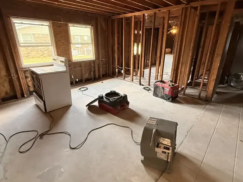 Dehumidifier and air movers drying a gutted room with open framing after water damage in Queens