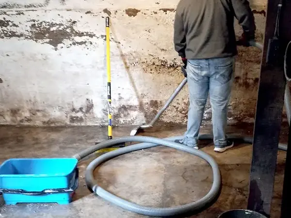 Extraction hose clearing water from a stained concrete basement floor in Queens