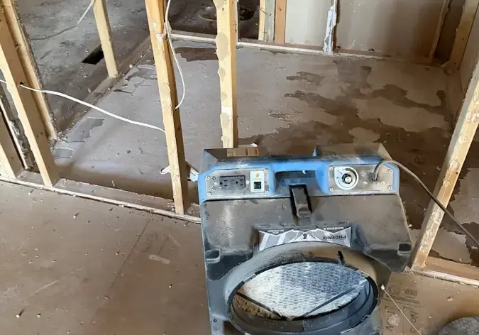 Air mover drying open wall framing and subfloor after water damage in Corona, NY